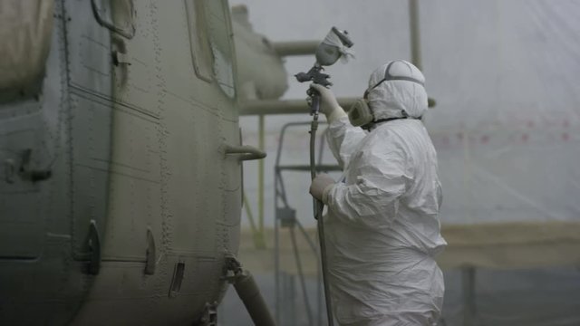 Worker Paints Helicopter Side with Sprayer in Hangar