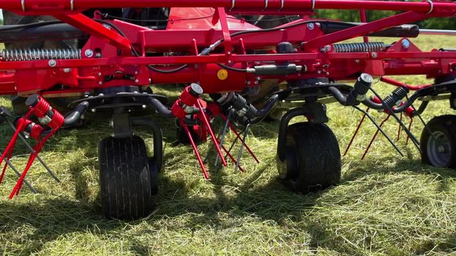 The wheels on the red rotary rakes machinery move to the right side. A farmer has pushed a button.
