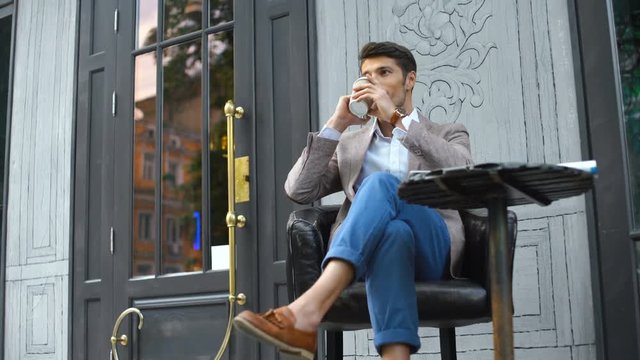 View from below of presentable man sitting by the table in cafe which talking on phone and drinking coffee