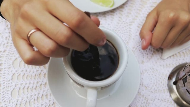 Female hand stirring coffee in the cup, top view