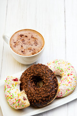 Cup of coffee and tasty donuts with icing and chocolate on white wooden background, copy space