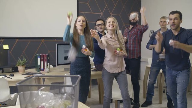 Group of coworkers throws paper into wastebasket