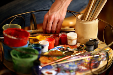 Artist painting on easel in studio. Cropped shot of hands paints of woman with brush. Indoor home interior for handmade crafts.