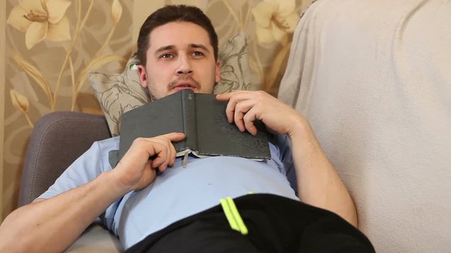 man reading a book lying on the couch and dreams