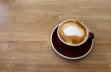 A cup of coffee with latte art in a brown cup on wooden table background