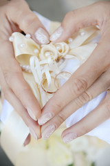 The hands of the newlyweds in the shape of a heart on a pillow with wedding rings