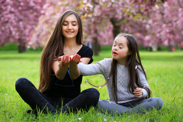 Happy beautiful young woman with girl in blossom park with trees and flowers.