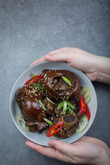 Braised pork hock in thick sauce garnished with scallions and red pepper. Gray background. 