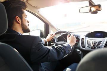 Handsome businessman  driving a car.Image taken from rear.