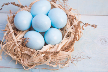 Blue Easter eggs in nest on wooden background.