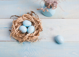 Blue Easter eggs in nest, vase with dry grass on wooden background.