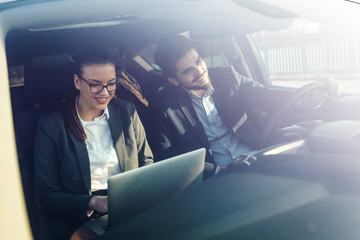 Two business friends in the car.They travel to business meeting.Man drives a car while female using laptop and preparing for presentation. 
