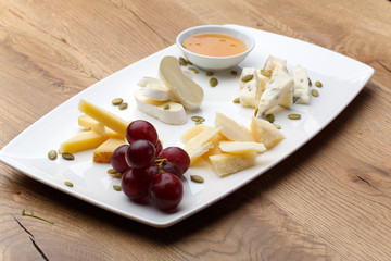 Different types of cheese with honey and grapes