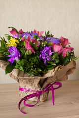Bouquet of flowers (Purple orchid, alstroemeria, green chrysanthemum, gypsophila and buxus) in paper with bow on wood.