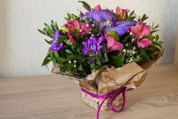 Bouquet of flowers (Purple orchid, alstroemeria, green chrysanthemum, gypsophila and buxus) in paper with bow on wood.