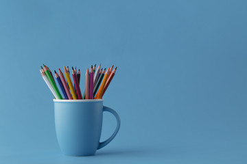 Full mug of sharp color pencils on monochromatic blue background