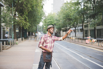 Knee figure of young handsome afro black man trying to call a taxi raising his hand in the city, overlooking left - transport concept