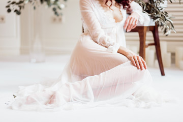 Fototapeta na wymiar girl with a beautiful figure in white boudoir dress sitting near the chair, legs close-up