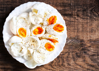 Hard boiled eggs, sliced in halves with black pepper spice on wooden background top view