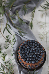 beautiful chocolate layered cake with open biscuits, decorated with fruit blueberries in a brown ceramic bowl on kitchen grey towel on white wooden background top view