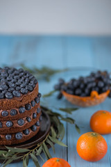 a beautiful cake decorated with blueberries and eucalyptus on brown ceramic dish blue wood background with orange tangerines closeup