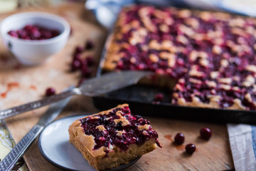 a piece of cake saucers cherry fruit pie on a black baking tray on wooden Board with white blue kitchen towels close-up