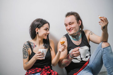 the guy with the girl in the tattoo in black shirts drink tea with croissant on white background...