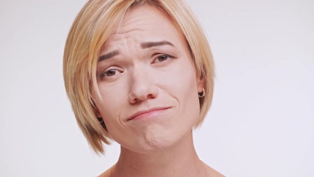 Confused middle-aged Caucasian woman with blonde hair looking at camera with upset. Close up footage on white background
