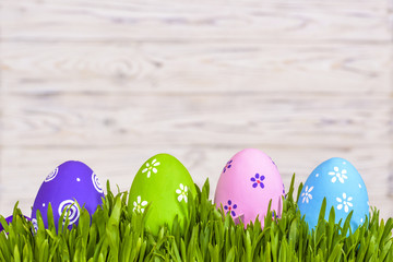 Pastel colored easter eggs in green grass over rustic wooden background.