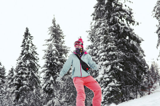 Look from below at woman in pink suit going down on the snowboard along the forest line