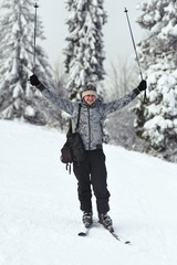 Fototapeta na wymiar Man in grey ski suit raises up his poles posing on white hill