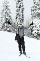 Fototapeta na wymiar Man in grey ski suit raises up his poles posing on white hill