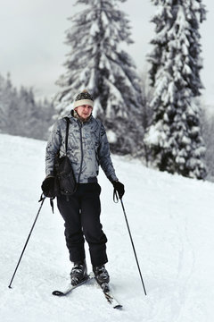 Man in grey ski suit stands on skis and holds the poles