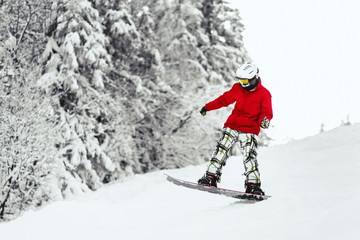 Man in red ski jacket goes down the hill on his snowboard