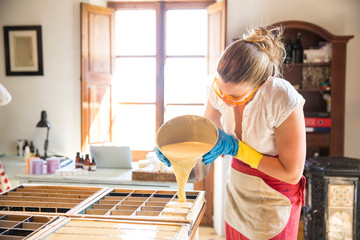 Young woman pouring liquid lavender soap into moulds in handmade soap workshop
