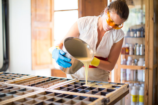 Young woman pouring liquid into soap mould in handmade soap workshop