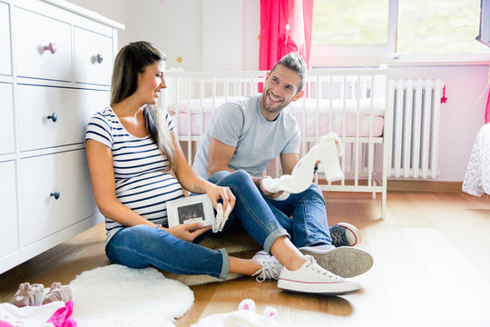 Pregnant couple sitting on floor in nursery preparing baby clothes