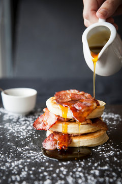 Female hand pouring maple syrup over breakfast bacon crumpet on slate