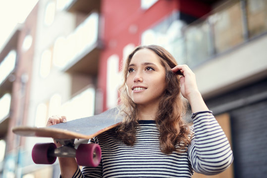 Young female skateboarder on street carrying skateboard on shoulder