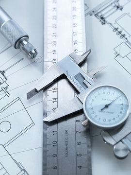 Dial calipers sitting on steel rule with engineering drawings