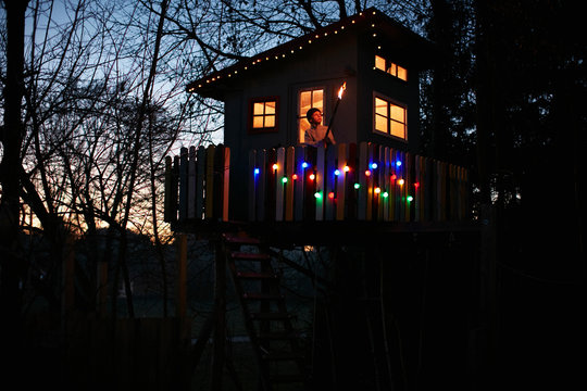 Boy With Flame Torch Looking Out From Treehouse Balcony At Night