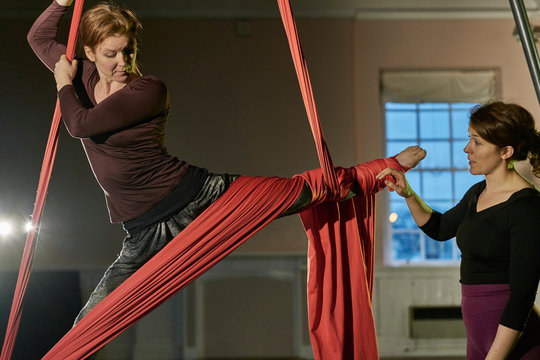 Two young female aerial acrobats practicing the splits on silk rope