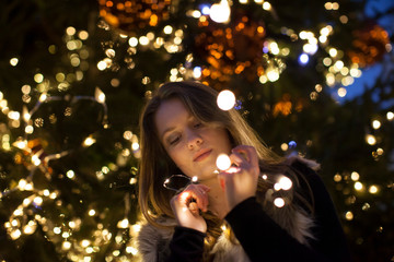 Young woman looking at lights in her hand, tree in background