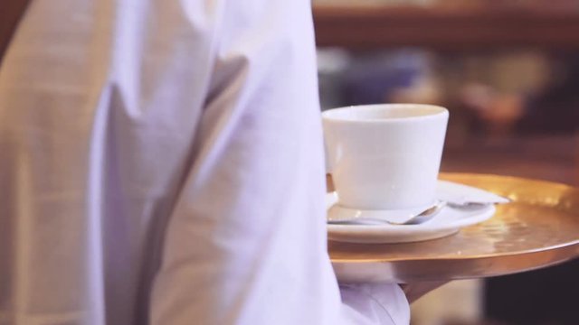 Back view of dark-skinned Waitress carrier cup of coffee for bearded man by the table