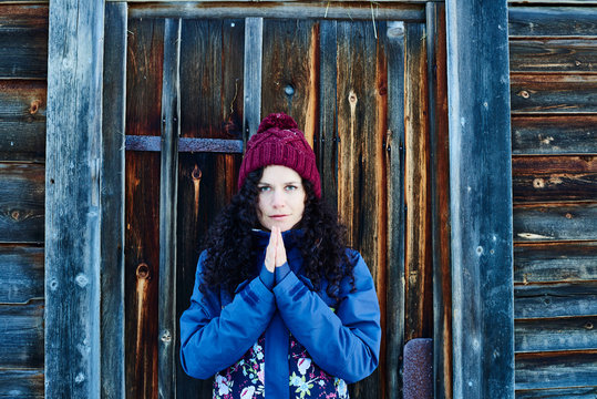 Portrait of woman in knit hat practicing yoga, meditating by log cabin door