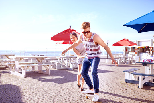 Couple Using Skateboard On Promenade