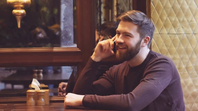 Bearded Man sitting in cafe by the table and talking on phone
