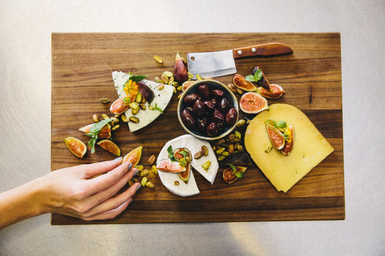 Variety cheese plate with figs, olives, pistachios, cleaver on wooden chopping board