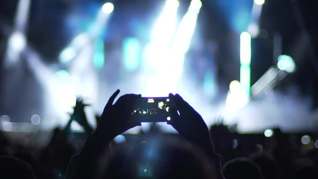 Hands of person taking picture of pop star performing on stage, crowd applauding