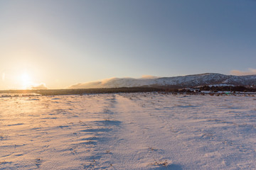 Winter road to the forest. Sunset landscape. Snow covered field.